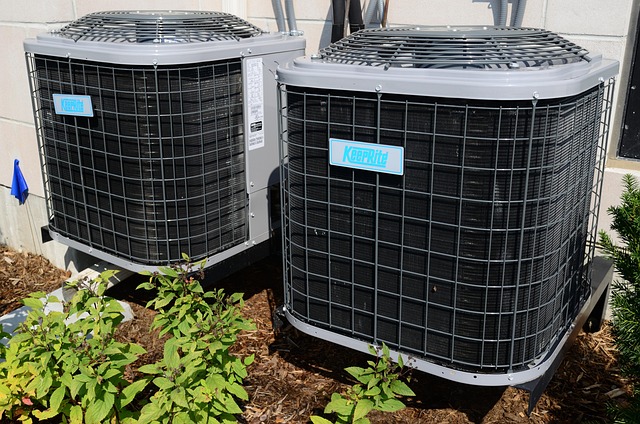 Two outdoor central air conditioning units installed beside a building with mulch and small shrubs, typical of a Monmouth County NJ commercial HVAC setup.