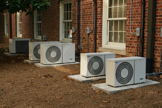 Multiple outdoor ductless mini-split condenser units installed along a brick building exterior, mounted on concrete pads with electrical connections visible.